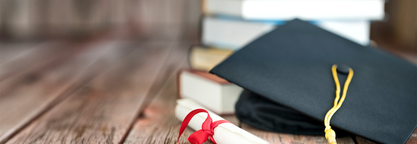 Books and a graduation cap on a wooden table